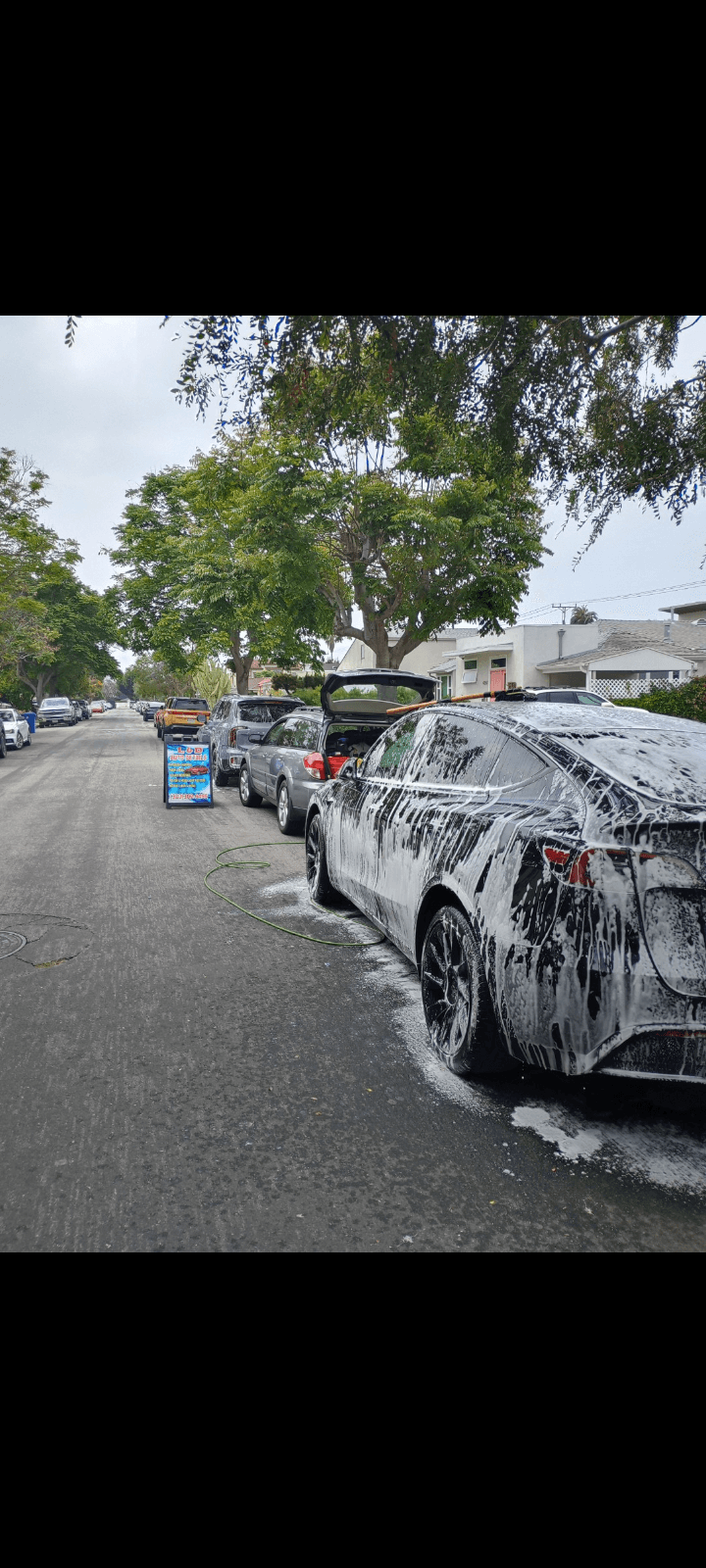 Tesla Model Y covered in cleaning foam during a street-side wash